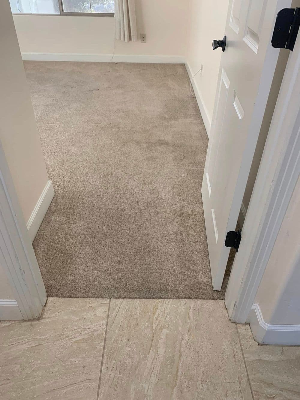 Neutral-colored carpet transitions to tiled floor near an open door in a well-lit room.