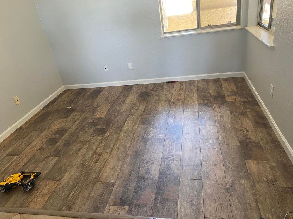 Renovated room with wood laminate flooring and a window, tools visible in the corner.