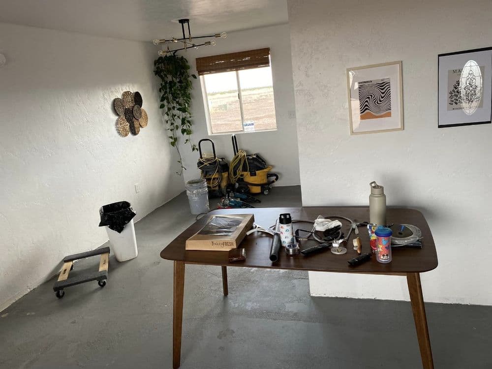 Modern room with a table, tools, decor, and cleaning equipment in a bright, minimalist space.