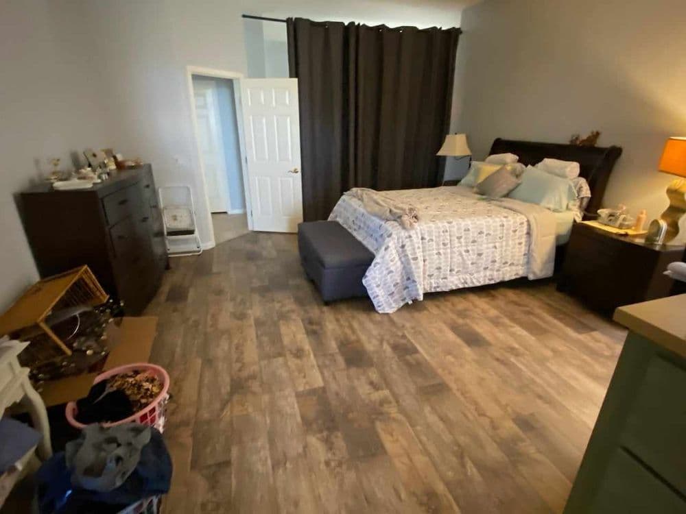 Spacious bedroom with a queen bed, dresser, and hardwood floors, featuring soft lighting.
